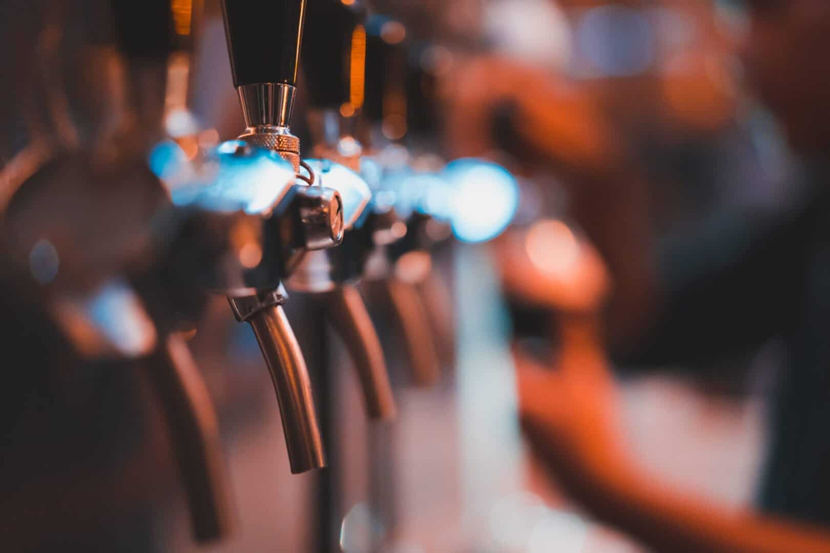 silver beer dispenser with blurred bartender poured cold draft beer into glass, selective focus, orange tone